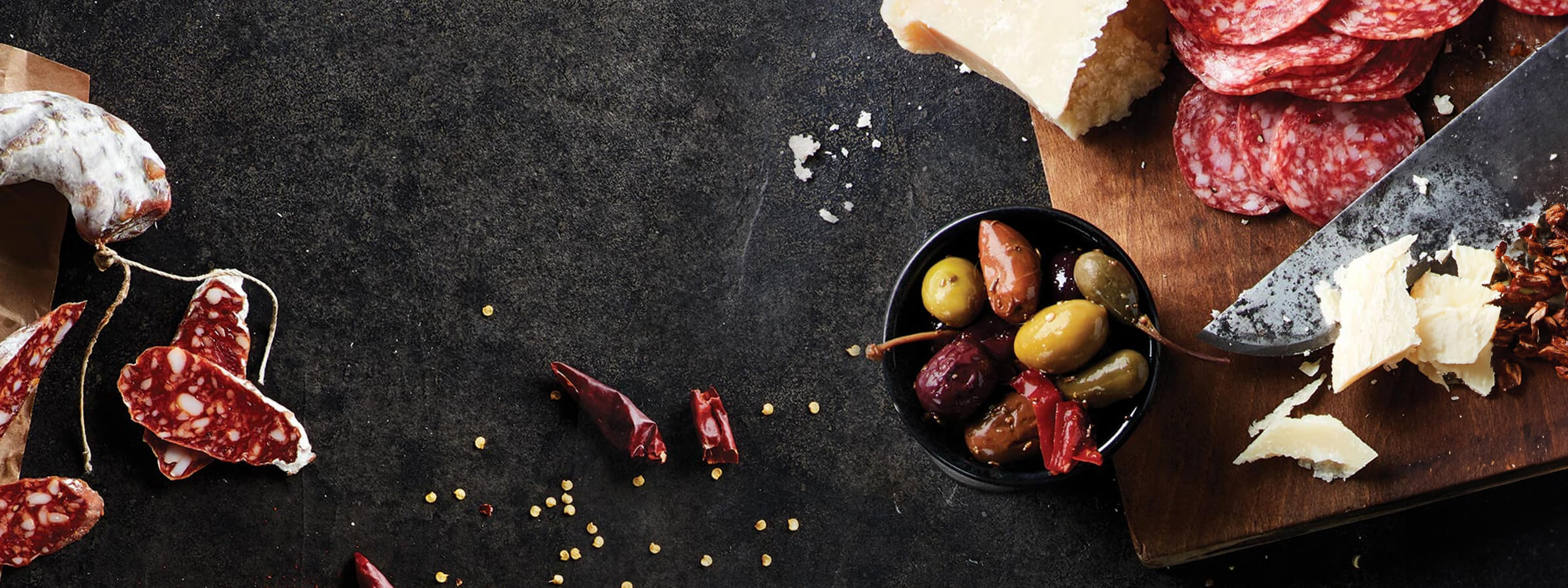 sliced Columbus meats with olives & cheese on a dark stone board